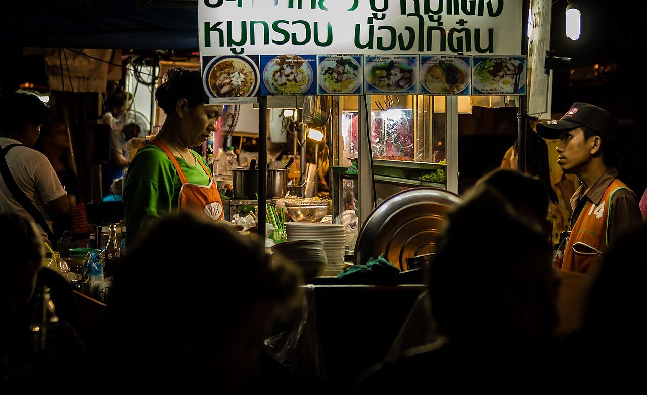 A street food stall at night in Bangkok, diners gathered around the counter