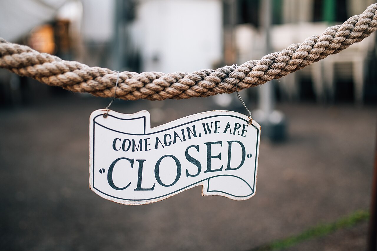 A 'Come Again, We Are Closed' sign hanging on a rope outside a restaurant